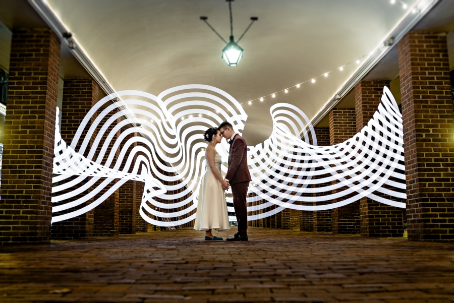 A man and woman hold hands in The Shambles in Philadelphia with light trails behind them.